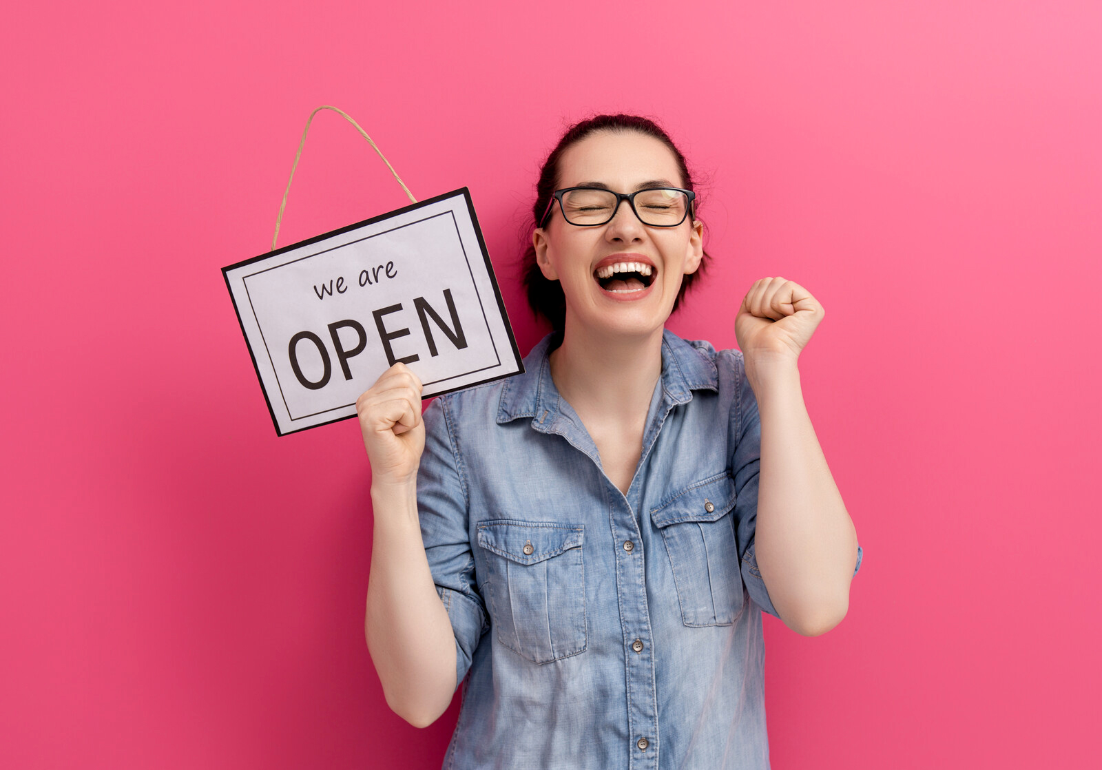 A happy woman holding an "open" sign with a pink background.