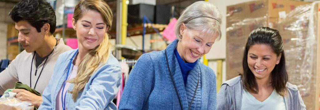 4 people of different ages and genders are working together in a warehouse.